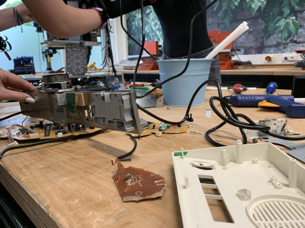 Close-up van een werkbank waarop een elektronisch apparaat is gedemonteerd, met zichtbare printplaten, kabels en losse onderdelen.