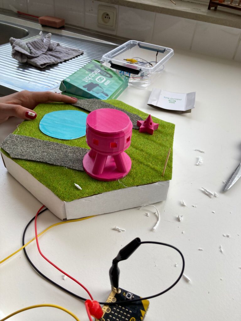 Technische maquette van een miniatuurstad op zeshoekige module, met gebouwen, wegen en aangesloten elektronica zoals draadjes en sensoren.