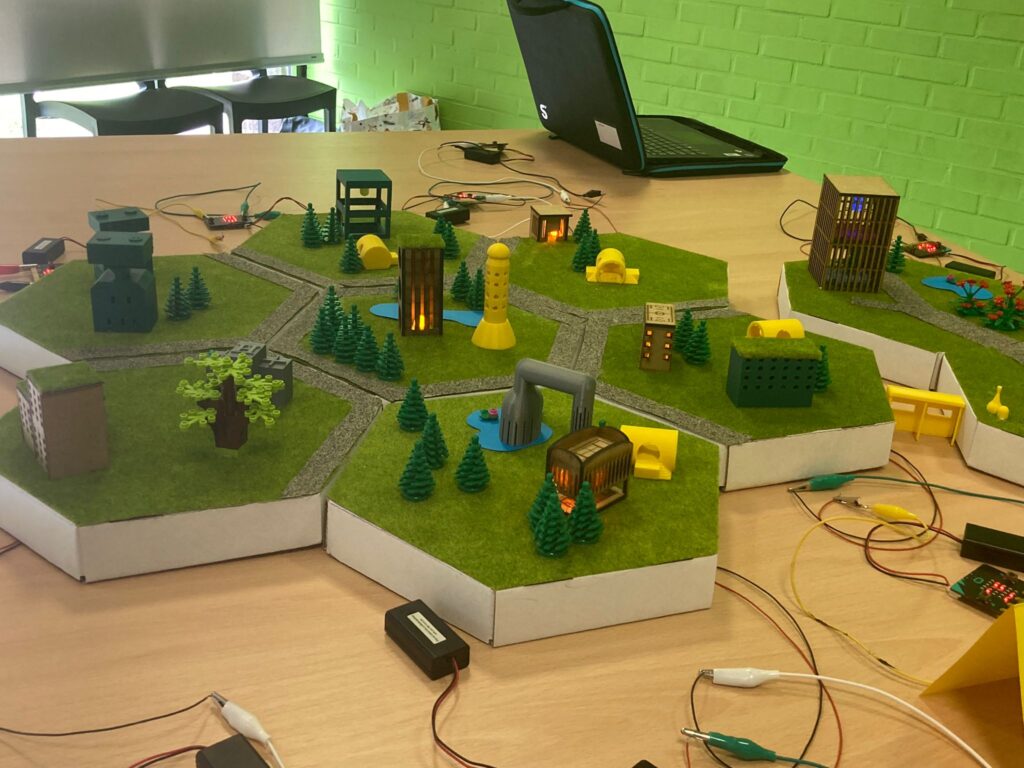 Technische maquette van een miniatuurstad op zeshoekige modules, met gebouwen, wegen, bomen en aangesloten elektronica zoals draadjes en sensoren.